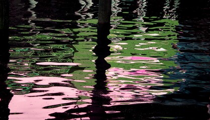 Photo of colors reflected in the water surrounded by pier post. 