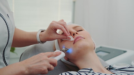 Close-up shot of Professional cosmetologist making cavitation peeling on young woman's face at beauty salon with modern equipment and pleasant atmosphere.