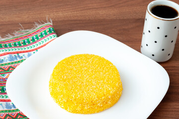 tasteful and colorful brazilian corn couscous served with a cup of coffee on a wooden table