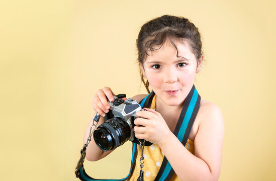 Little girl with funny cute expression holding old film camera on yellow background