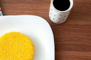 tasteful and colorful brazilian corn couscous served with a cup of coffee on a wooden table