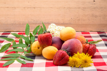 Strawberries, peach, apricot, rowan flower, yellow dandelion lie on the table on the tablecloth