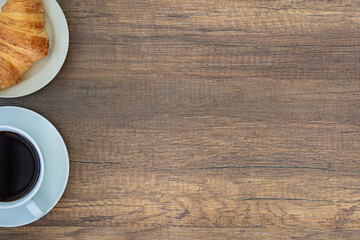 Top view of a desk with a cup of coffee and croissants on a wooden table.