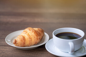 Side view of a desk with a cup of coffee and croissants on a wooden table.