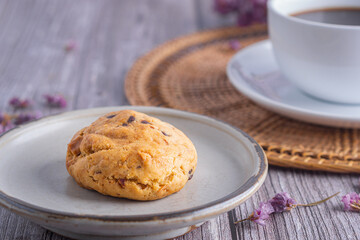 Close-up of a cookie on a plate with a white coffee cup and flower blurred background.