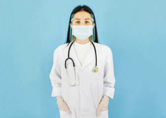 Smart young asian female doctor in lab coat with Medical face mask,white latex medical gloves,face Shield and stethoscope against blue background,health care concept