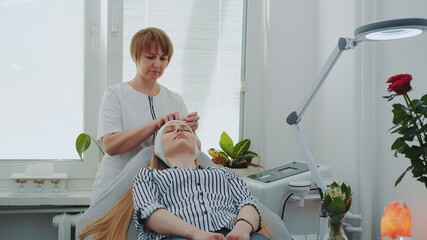 Beautician preparing woman for making facial cleansing in beauty salon. Woman resting after hard working week.