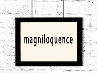 Black frame hanging on white brick wall with inscription magniloquence