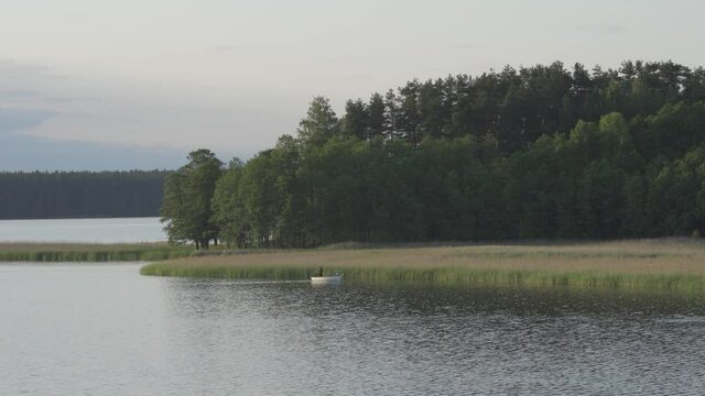 Two anglers in wooden boat sailing on lake, telephoto static shot, Wigry National Park, Suwalszczyzna, Poland,