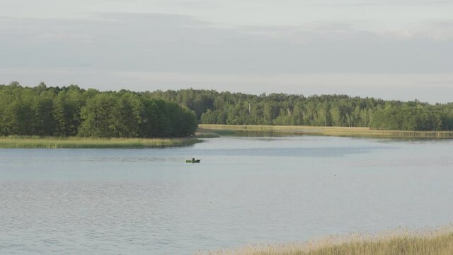 Single man rowing wooden boat with aors through middle of lake, telephoto static shot, Wigry National Park, Suwalszczyzna, Poland