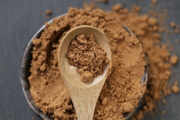 Guarana powder in a wooden spoon and a ceramic cup on a black slate background.Brown shredded guarana powder texture. .Natural energetic.Useful product.