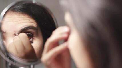 Young brunette woman plucks her eyebrows with tweezers in front of the mirror at home. close up. - Powered by Adobe
