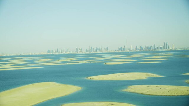 Unseen amazing view of the worls island in Dubai. Helicopter shoot coming from low angle wide and showing the islands plus teh Dubai city and skyline in the background during day time