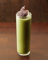 matcha green tea iced latte with red bean azuki anko on rustic wood table and wall