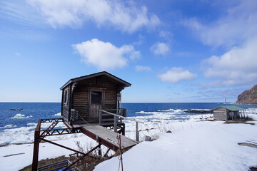 Rustic wood cabin on a snowy beach in Hokkaido with Sea ice on the shoreline. © Dane