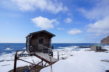 Rustic wood cabin on a snowy beach in Hokkaido with Sea ice on the shoreline.