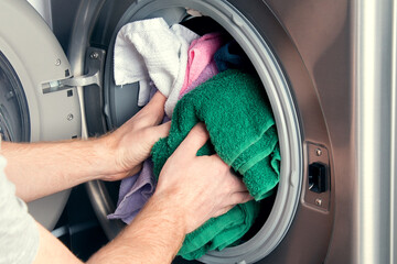Man taking color clothes from washing machine. A drum of washing machine full of dirty laundry in...
