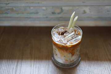 Iced Latte - A glass of coffee with fresh milk and lemongrass on table and blurred background, Perfect drink for summer time.