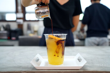 Iced coffee with orange - A plastic glass of espresso shot mixed with orange juice and craft soda on blurred background, Barista making coffee cocktail, Perfect drink for summer time.