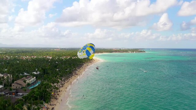 Picturesque view of two people parasailing in yellow and blue parachute by sandy Punta Cana beach, Dominican Republic, aerial