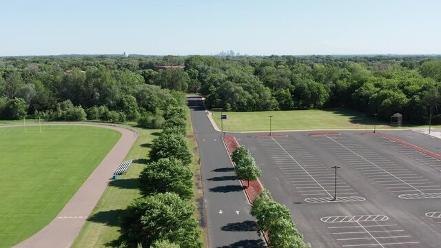 Aerial descending shot above school parking lot and athletic track with Minneapolis skyline in the background. 4K