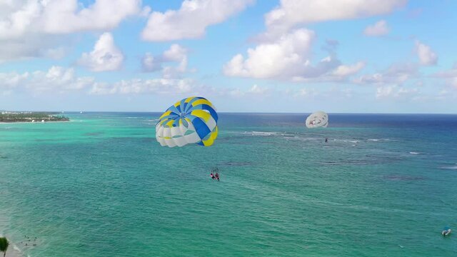 Scenic view of two people parasailing together in yellow and blue parachute by sandy Punta Cana resort beach, Dominican Republic, aerial