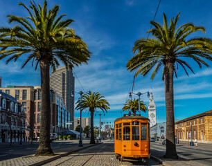 Old orange San Francisco cable car on the Embrcadero with the Ferry Building and palm trees in the...