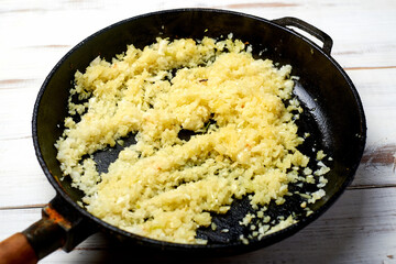 Fried onions in a pan on a light wooden background. Preparation for cooking.