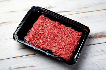 Minced meat in packaging on a light wooden background.