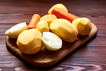 peeled raw potatoes, carrots, onions on a wooden background. Preparing vegetables for cooking.