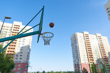 A basketball basket and a shield for street basketball against the background of modern residential buildings. Exercise in the fresh air with the ball. Basketball training.