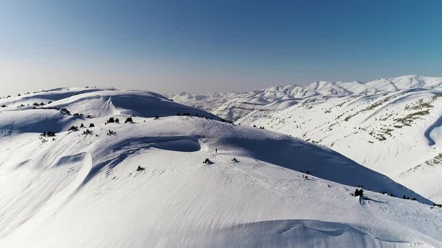 Sensational flight above white snow covered Akoura mountain ridge towards bright blue sky and range, Lebanon, overhead aerial approach