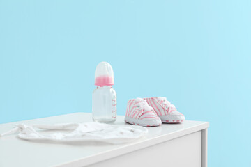 Baby shoes with bottle and bib on chest of drawers in room