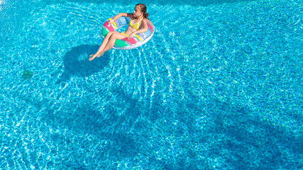 Acrive girl in swimming pool aerial top view from above, kid swims on inflatable ring donut , child has fun in blue water on family vacation resort
