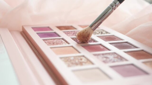 Make up artist is dipping her make up brush into glitter in pink eyeshadow palette, in slow motion