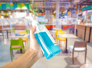 Hand holding blue alcohol gel sanitizer liquid bottle,Alcohol gel for cleaning hand to protect corona virus(covit-19) on blur food court center background .