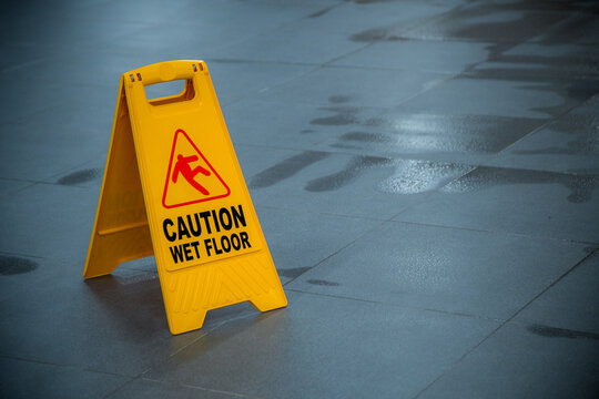 Yellow wet floor caution sign during rain with puddle of water when floor is slippery and copy space for text
