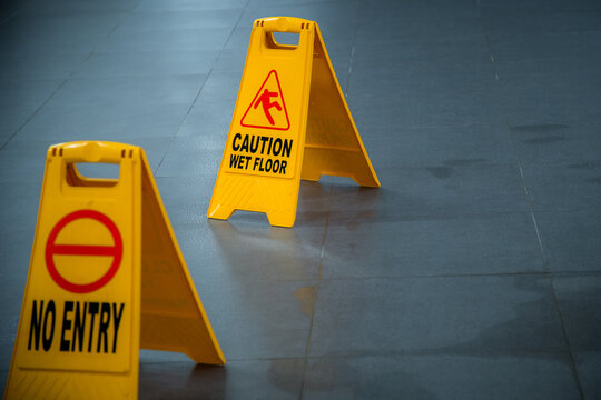 Yellow wet floor caution sign during rain with puddle of water when floor is slippery and copy space for text
