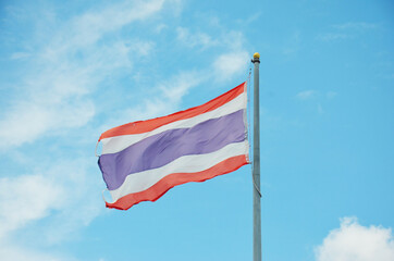 The flag of Thailand is atop a pole with a background in the sky.