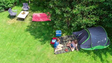 Aerial top view of campsite from above, mother and daughter having fun, tent and camping equipment...