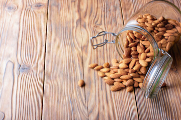 Almonds in a glass jar scattered on an old wooden table in cracks. Photo, image.