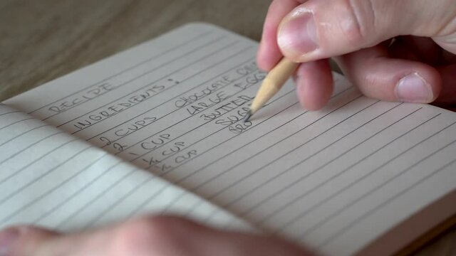 Hand of white man writing down recipe in notebook with pencil.
