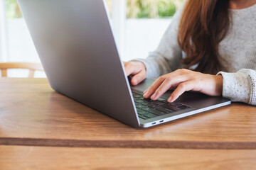 Closeup image of a woman working and typing on laptop computer keyboard on wooden table