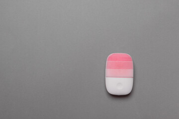 pink electric face massager on grey colored paper background, top view with copy space