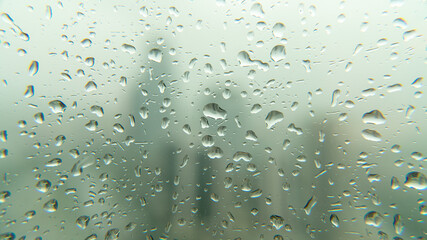Drops of rain on window glass with blurred skyscraper financial district city skyline.