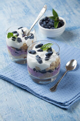 two glasses with cakes with cottage cheese cream, honeysuckle berries, mint leaves stand on a blue background and a blue napkin