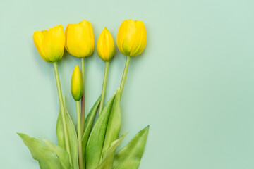 Naklejka premium Yellow tulip flowers bouquet on mint background. Flat lay, top view. Minimal floral concept. Spring flowers, floral background with copyspace