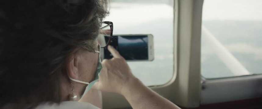 Woman with face mask takes a picture with smartphone in cockpit of small airplane plane aircraft staycation local travel during virus covid 19 coronavirus pandemic outbreak new normal