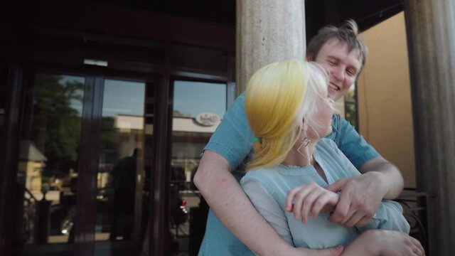 A guy and a girl standing at the entrance to the hotel communicate, hug and kiss. The girl has long yellow hair.