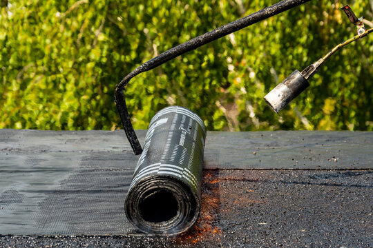 The builder puts waterproofing material on the roof of a multi-story residential building using a gas burner. Overhaul of the roof of the house.
